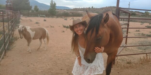Woman smiling with two horses in corral.