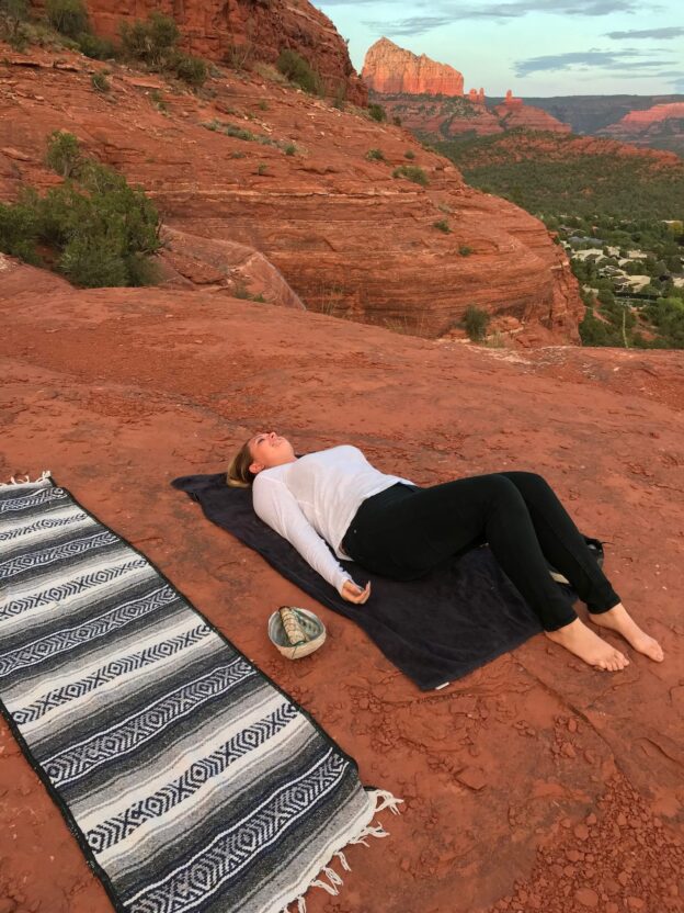 Person meditating on red rock landscape.