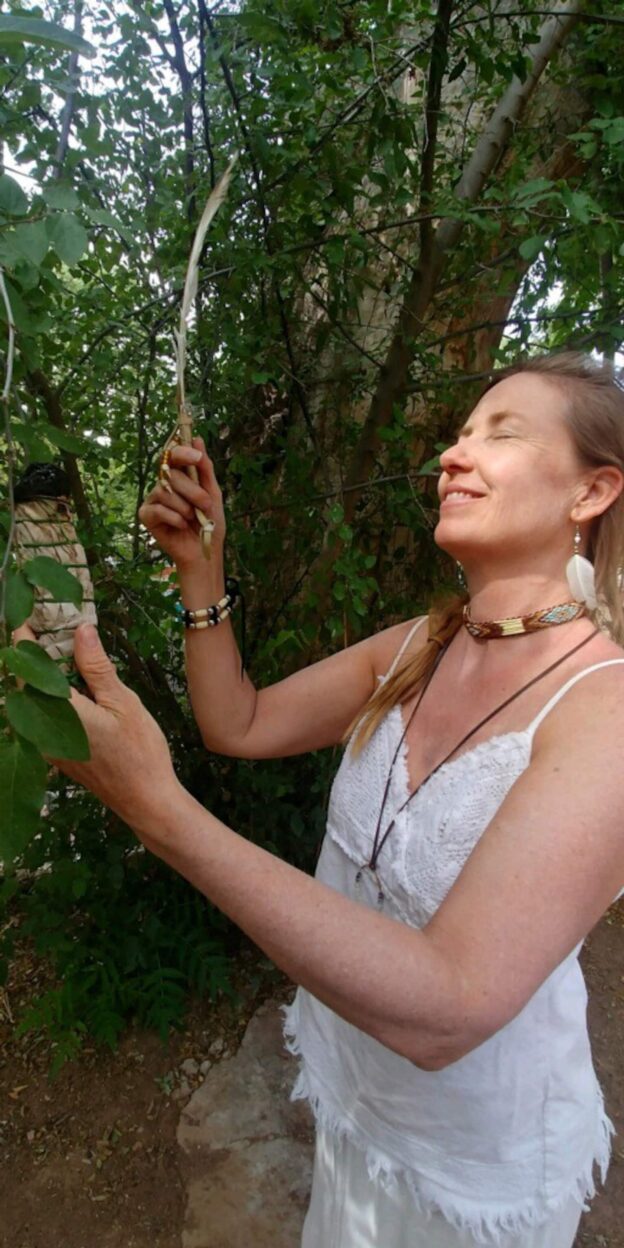 Woman smiling and holding a feather outdoors.